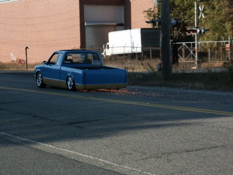 2001 Mercury Grand Marquis - A blue and tan pickup truck is seen from the rear, with sparks trailing from its undercarriage as it drives down a road.