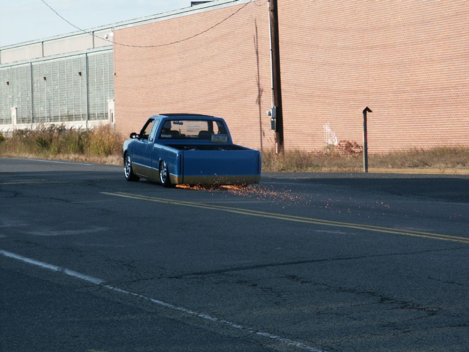 Blue pickup truck with gold trim driving on a road, sparks flying from the rear