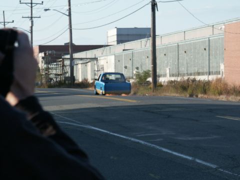 2001 Mercury Grand Marquis - A blue pickup truck drives away on a road, with industrial buildings in the background.