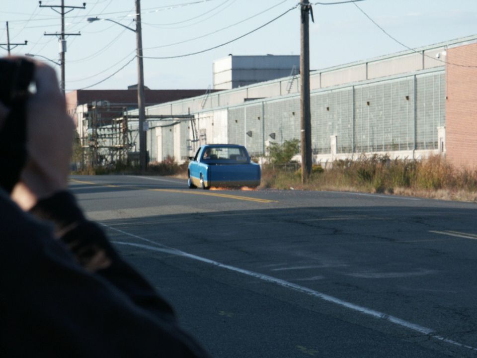 Blue pickup truck with yellow trim on the rear bumper, seen from behind on a road