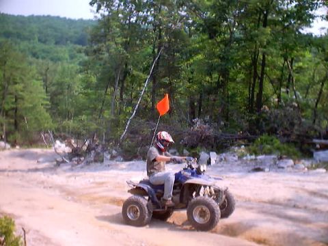 2001 Ford Escape - Rider on a blue ATV navigates a dirt path in a wooded area, with an orange flag for visibility.