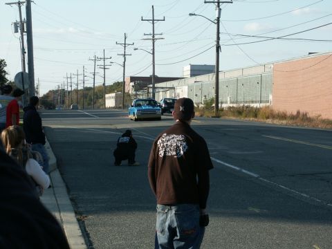 2001 Mercury Grand Marquis - Cars drive down a street as onlookers gather to watch.