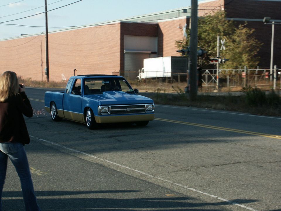 Blue and tan pickup truck with a lowered stance and aftermarket hood, driving on a road