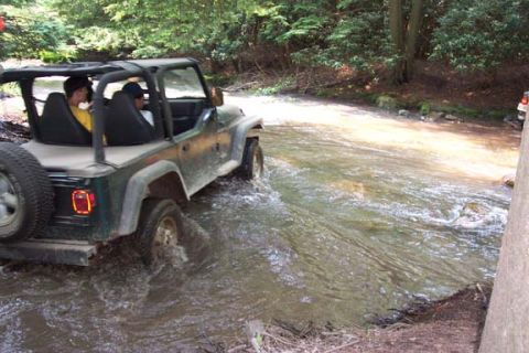 2001 Ford Escape - A Jeep Wrangler navigates a water crossing in a wooded area.