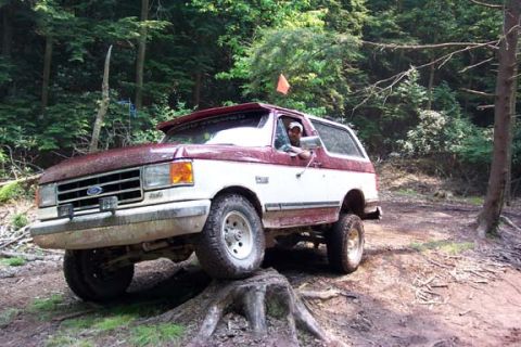 2001 Ford Escape - A two-tone red and white Ford Bronco navigates an off-road trail through a wooded area.