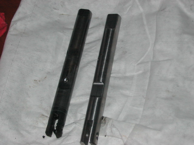 Two metal shafts, one looks worn and damaged at the end, lying on a white cloth