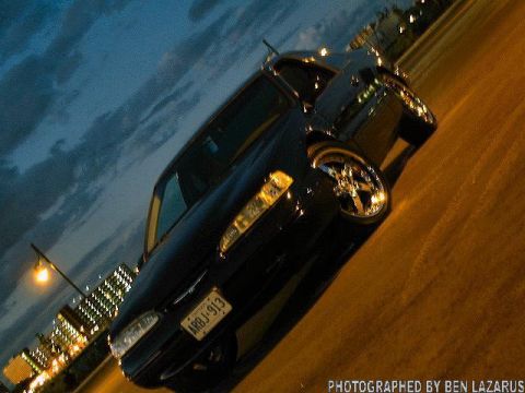 1997 Ford Thunderbird - A black sedan with chrome rims is parked on a street at twilight, with city lights visible.