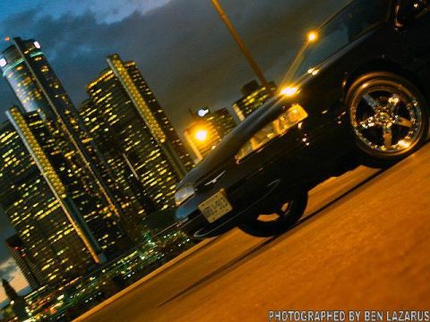 1997 Ford Thunderbird - A black 1997 Ford Thunderbird is parked on a road at night, with a city skyline illuminated in the background.