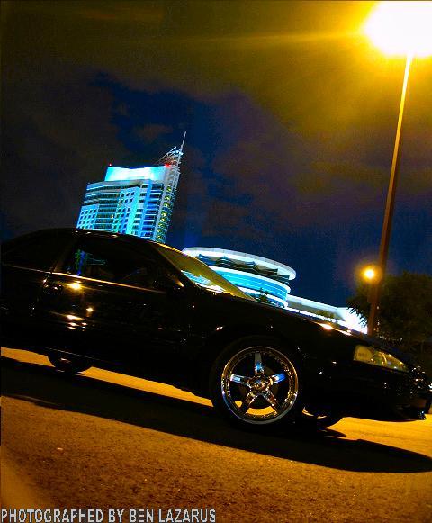 1997 Ford Thunderbird - A black 1997 Ford Thunderbird is captured at a 3q-front angle under a streetlamp at night, with a modern building in the background.