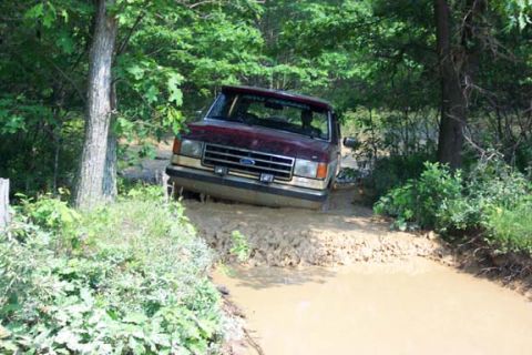 2001 Ford Escape - A maroon Ford truck navigates a muddy trail, its front end partially submerged.