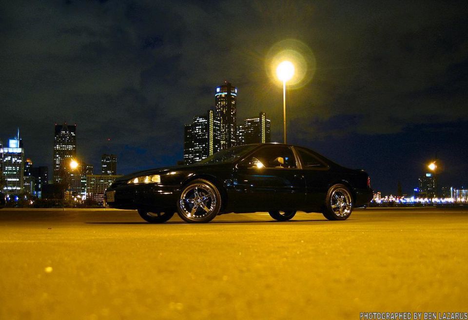 Black coupe parked at night with city lights in the background