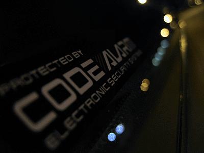 1997 Ford Thunderbird - A close-up of a car door shows a "CODE ALARM" sticker, with blurred lights reflecting on the surface.