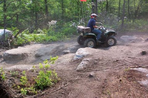 2001 Ford Escape - An ATV navigates a rocky, wooded trail with a rider wearing a helmet.