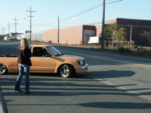 2001 Mercury Grand Marquis - A woman photographs a lowered Toyota Tacoma pickup truck on a sunny day.