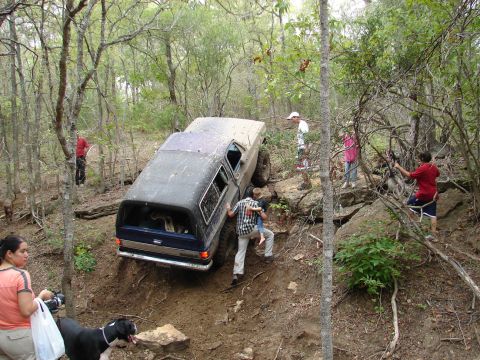 1996 Ford Bronco - People help a dark blue and grey SUV navigate a challenging muddy incline in a wooded area.