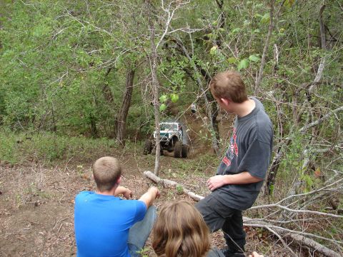 1996 Ford Bronco - People watch an off-road vehicle navigate a steep, wooded trail.