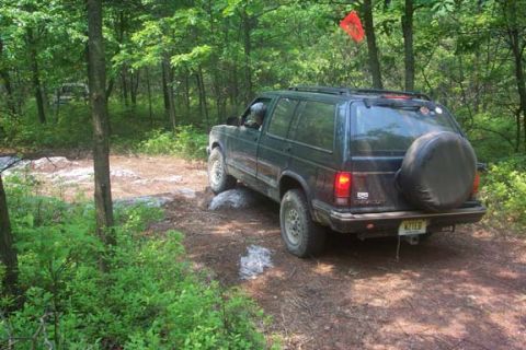 2001 Ford Escape - A dark SUV navigates a rocky, wooded trail, with a spare tire mounted on the rear.