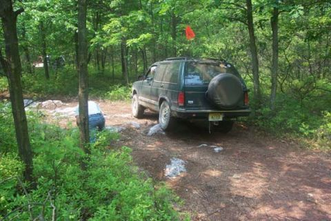 2001 Ford Escape - A dark green SUV navigates a wooded trail, its spare tire mounted on the back.
