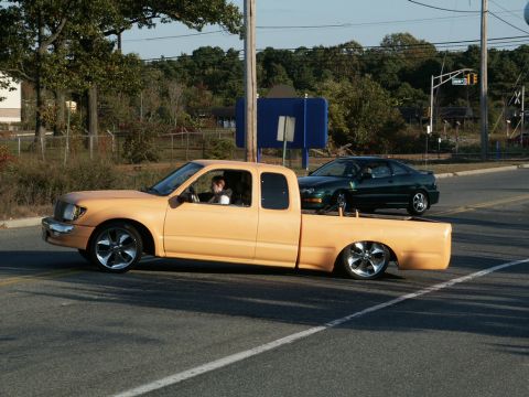 2001 Mercury Grand Marquis - A modified orange Toyota Tacoma pickup truck is seen driving on a road with a green car following behind.
