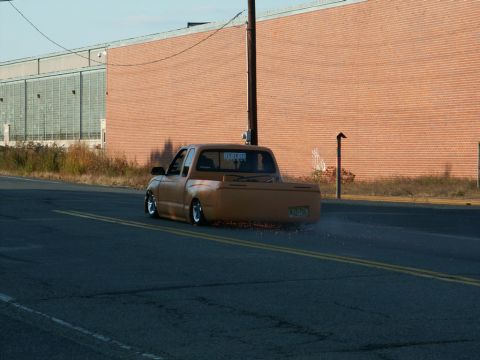 2001 Mercury Grand Marquis - An orange pickup truck with a slammed suspension is seen driving on a road, creating dust clouds from its tires.