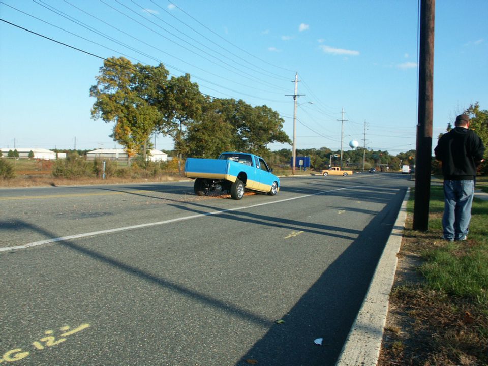 Blue and tan pickup truck with a lifted rear end, seen from a 3/4 front angle on a road