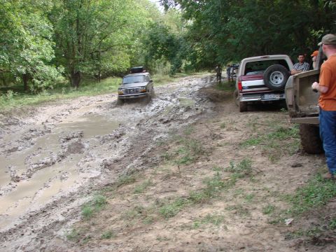 1996 Ford Bronco - A 1996 Ford Bronco navigates a muddy off-road trail, with other vehicles visible in the background.