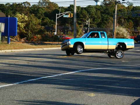 2001 Mercury Grand Marquis - A two-tone pickup truck performs a wheelie while driving through an intersection.