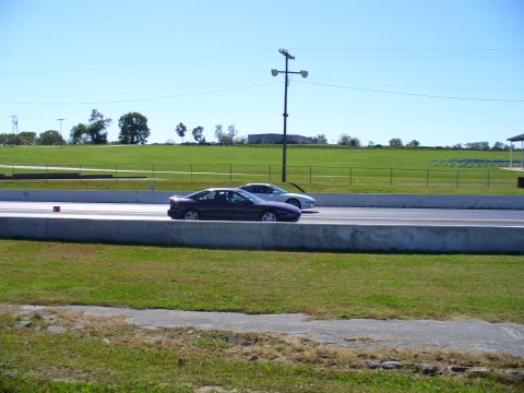 1991 Ford Probe - Two cars race down a drag strip on a sunny day, with a grassy field and trees in the background.