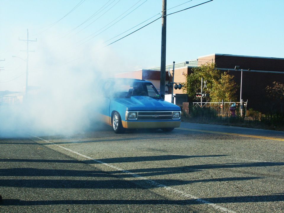 Blue and tan pickup truck with a lowered stance and aftermarket hood doing a burnout, emitting thick white smoke