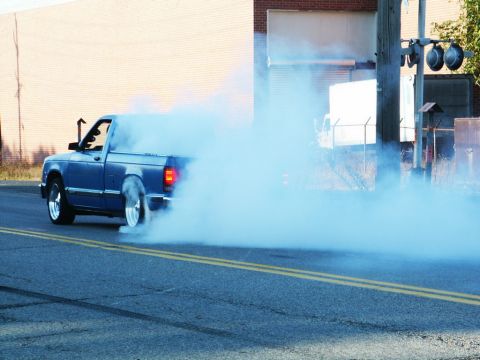 2001 Mercury Grand Marquis - A blue pickup truck creates a large cloud of smoke while performing a burnout on a street.
