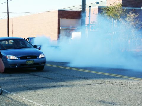 2001 Mercury Grand Marquis - A blue Ford Taurus is performing a burnout, creating a large cloud of smoke. Another vehicle is visible behind it.