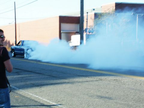 2001 Mercury Grand Marquis - A blue pickup truck performs a burnout, creating a massive smoke cloud on the road.