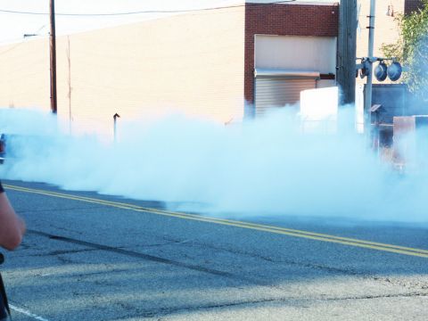2001 Mercury Grand Marquis - A car performs a burnout, creating a massive plume of blue smoke that obscures the road and surrounding buildings.