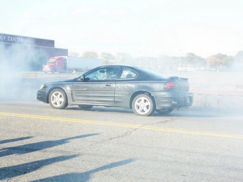 2001 Mercury Grand Marquis - Pontiac Grand Am performing a burnout with smoke covering the rear of the vehicle.