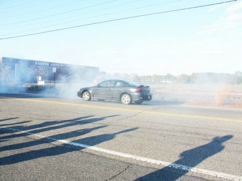 2001 Mercury Grand Marquis - A gray Pontiac Grand Prix is seen kicking up smoke while driving past a building.