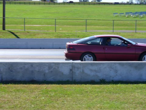 1991 Ford Probe - A red coupe with a distinctive sloping roofline is captured in profile on a race track.