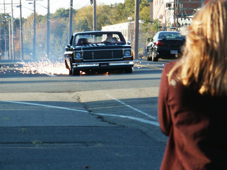 1973 Chevrolet C10 pickup truck doing a burnout, sparks flying from rear wheel. Another car is behind it