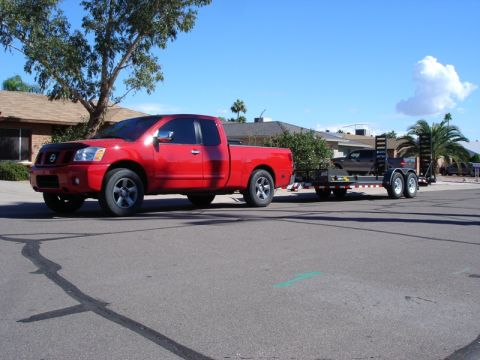 2005 Nissan Titan - A red 2005 Nissan Titan pickup truck is seen from the side, towing a trailer with a car on it.