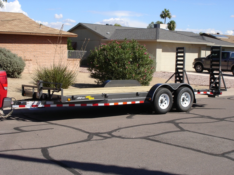 Black tandem-axle car hauler trailer with wood deck and upright ramps in a driveway