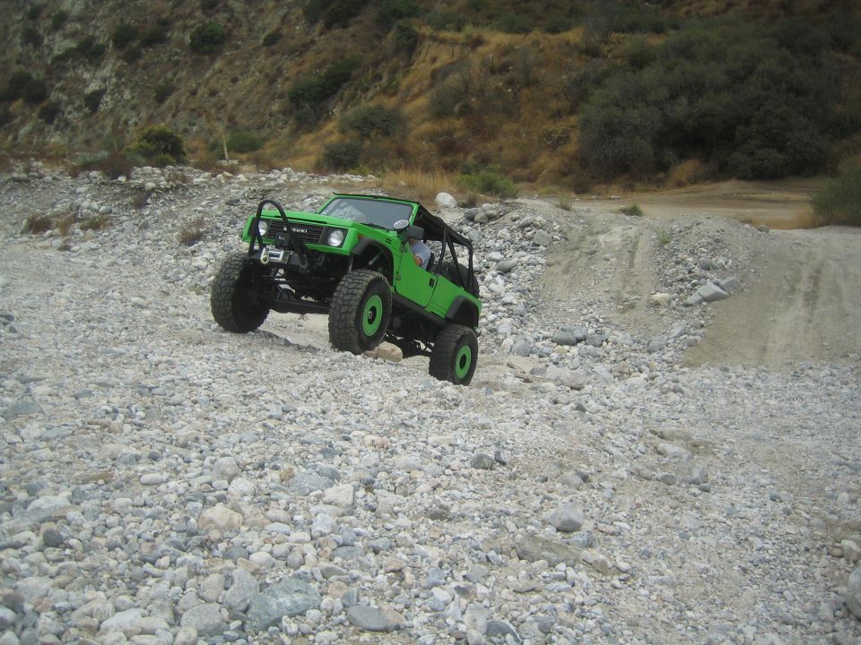 Green 1987 Suzuki Samurai climbing a rocky hill. It has large off-road tires and a winch