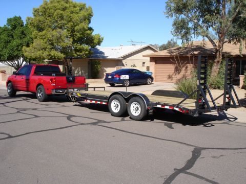 2005 Nissan Titan - A red 2005 Nissan Titan pickup truck is seen from the rear, towing a large flatbed trailer.