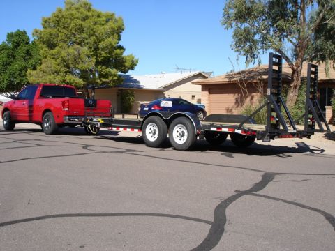 2005 Nissan Titan - A red Nissan Titan pickup truck is seen towing a car on a trailer down a residential street.