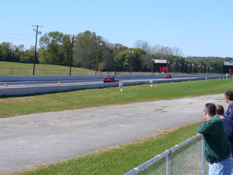 1991 Ford Probe - Two cars compete on a drag strip under a clear sky, with spectators watching from the side.