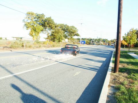 2001 Mercury Grand Marquis - A black pickup truck drives down a road, kicking up dust and debris from the shoulder.