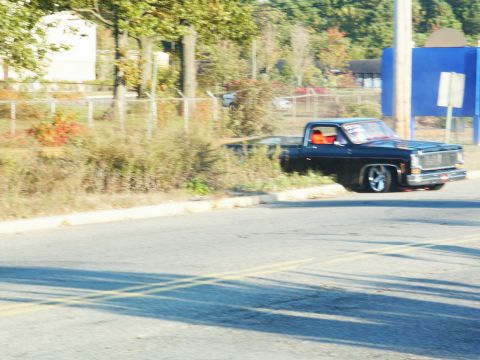 2001 Mercury Grand Marquis - Customized black pickup truck driving on a road with trees and buildings in the background.