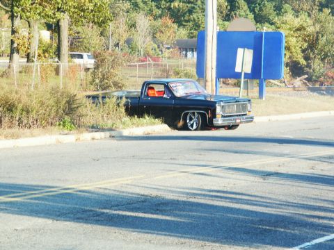 2001 Mercury Grand Marquis - A customized black pickup truck sits low to the ground, parked near some bushes and a utility pole.