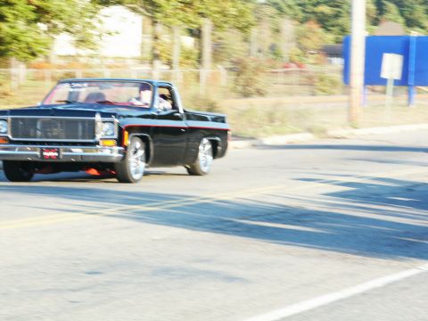 2001 Mercury Grand Marquis - Customized black pickup truck with red stripe and chrome wheels seen on the road.