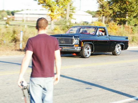 2001 Mercury Grand Marquis - A black pickup truck with custom wheels is seen driving on a road, with a person walking in the foreground.