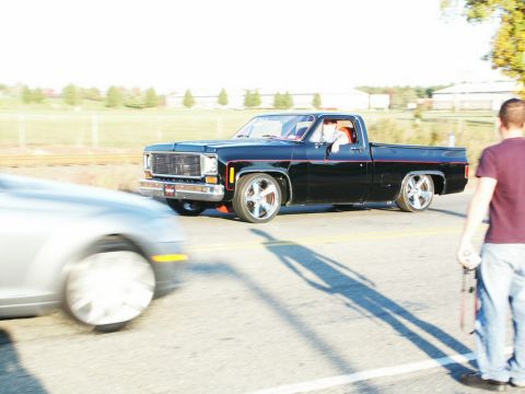 2001 Mercury Grand Marquis - A black pickup truck drives past a silver car on a sunny day.