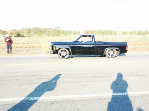 2001 Mercury Grand Marquis - Side view of a black pickup truck driving on a road with custom wheels.